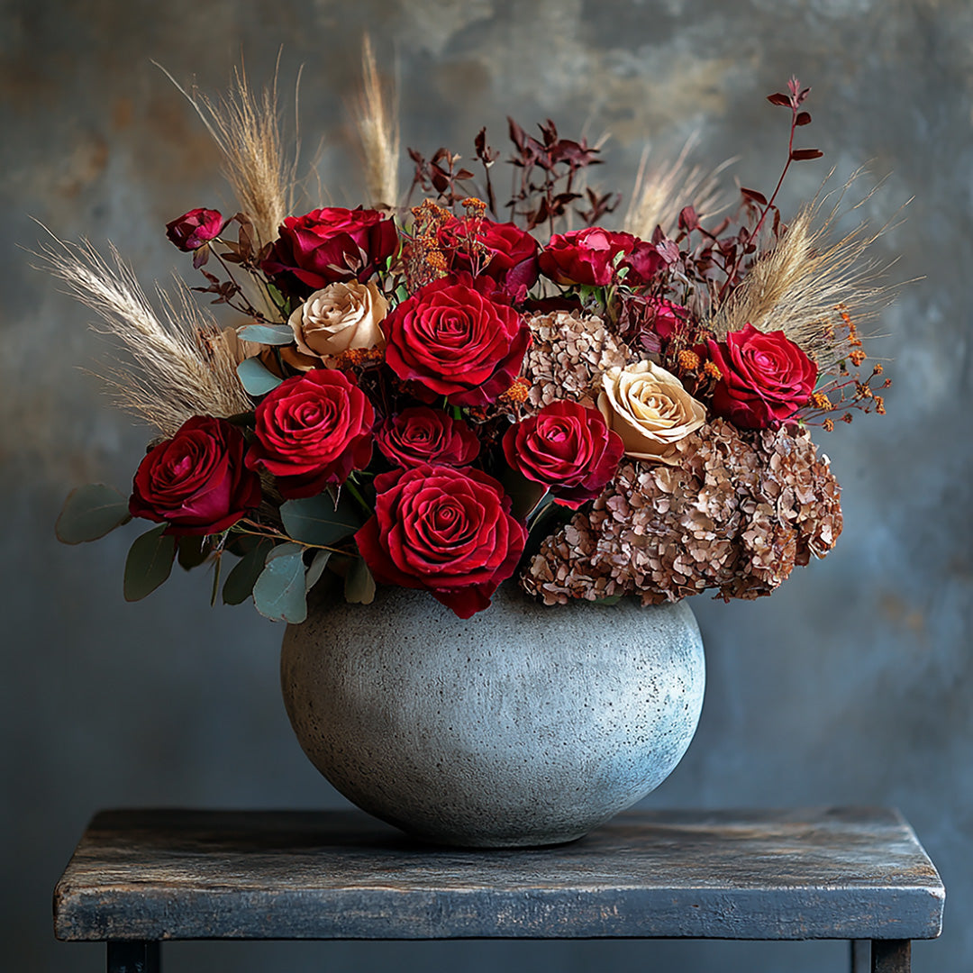 A luxurious and elegant floral arrangement featuring rich red roses, soft cream roses, dried florals, and pampas grass. This beautifully balanced bouquet, presented in a textured ceramic vase, evokes a sophisticated, timeless charm, perfect for special occasions or a heartfelt gift.