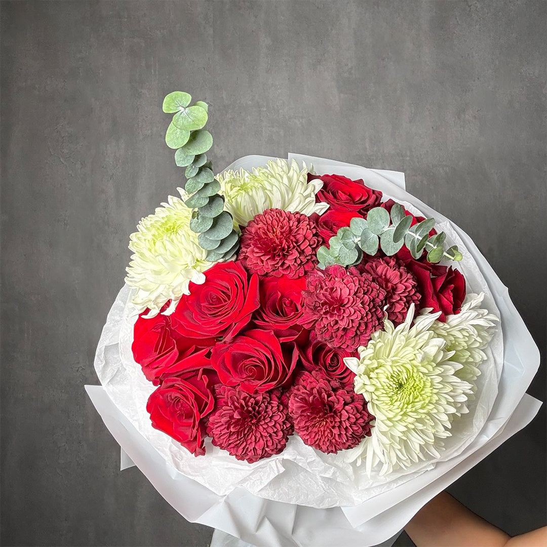 Handcrafted bouquet of red roses, burgundy and white chrysanthemums with eucalyptus foliage, wrapped in white tissue paper.
