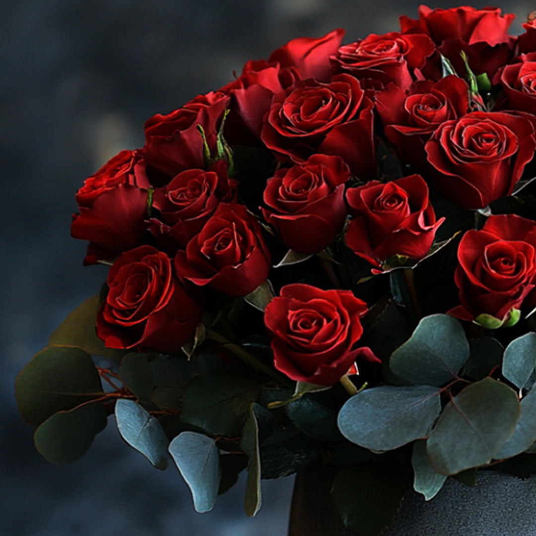 A close-up of a luxurious red rose bouquet, elegantly arranged with deep, rich red roses and surrounded by fresh eucalyptus leaves, creating a romantic and sophisticated floral display perfect for any occasion.