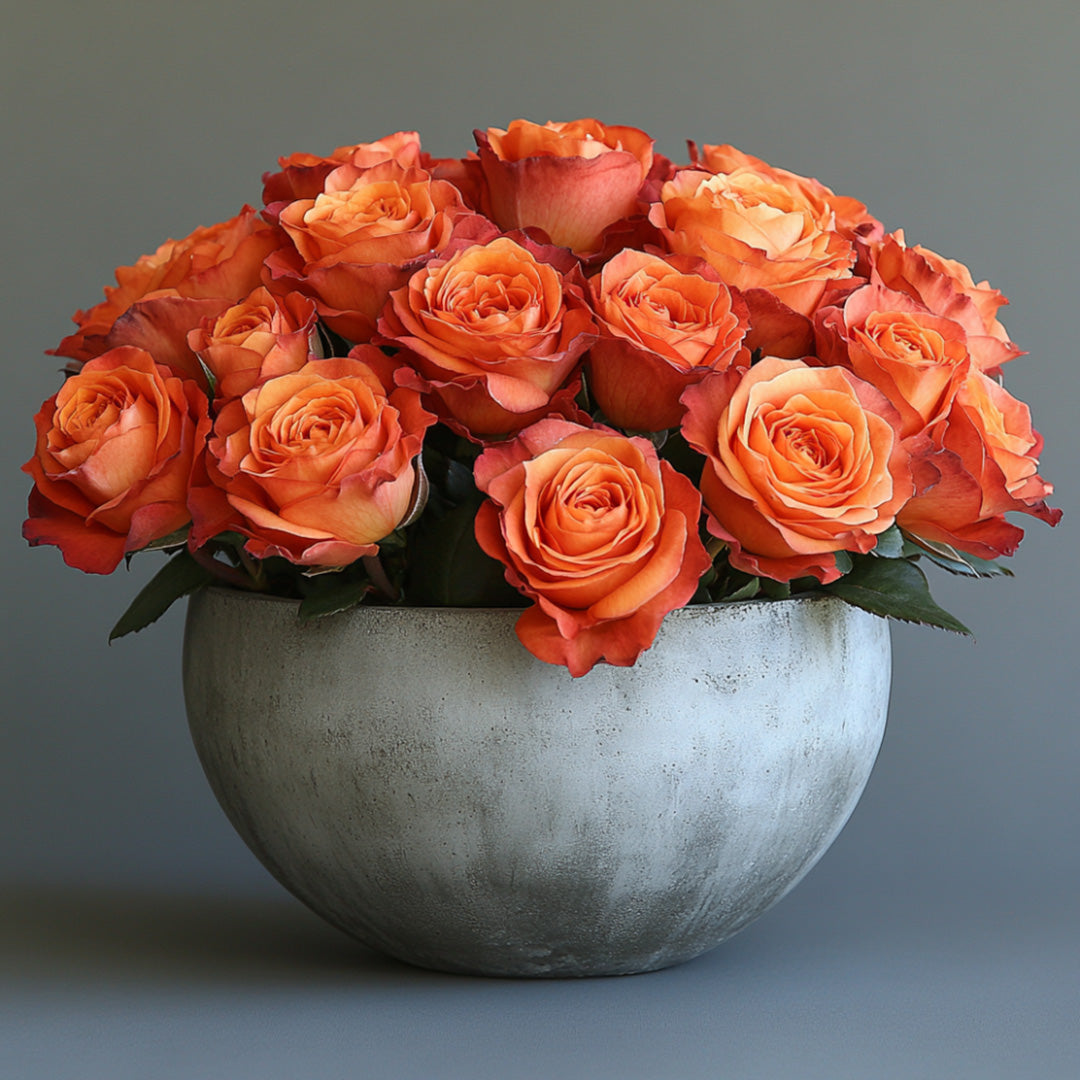 A stunning bouquet of vibrant orange roses arranged in a smooth, modern gray ceramic vase. The roses showcase a soft gradient of peach to orange, creating a warm and inviting appearance.