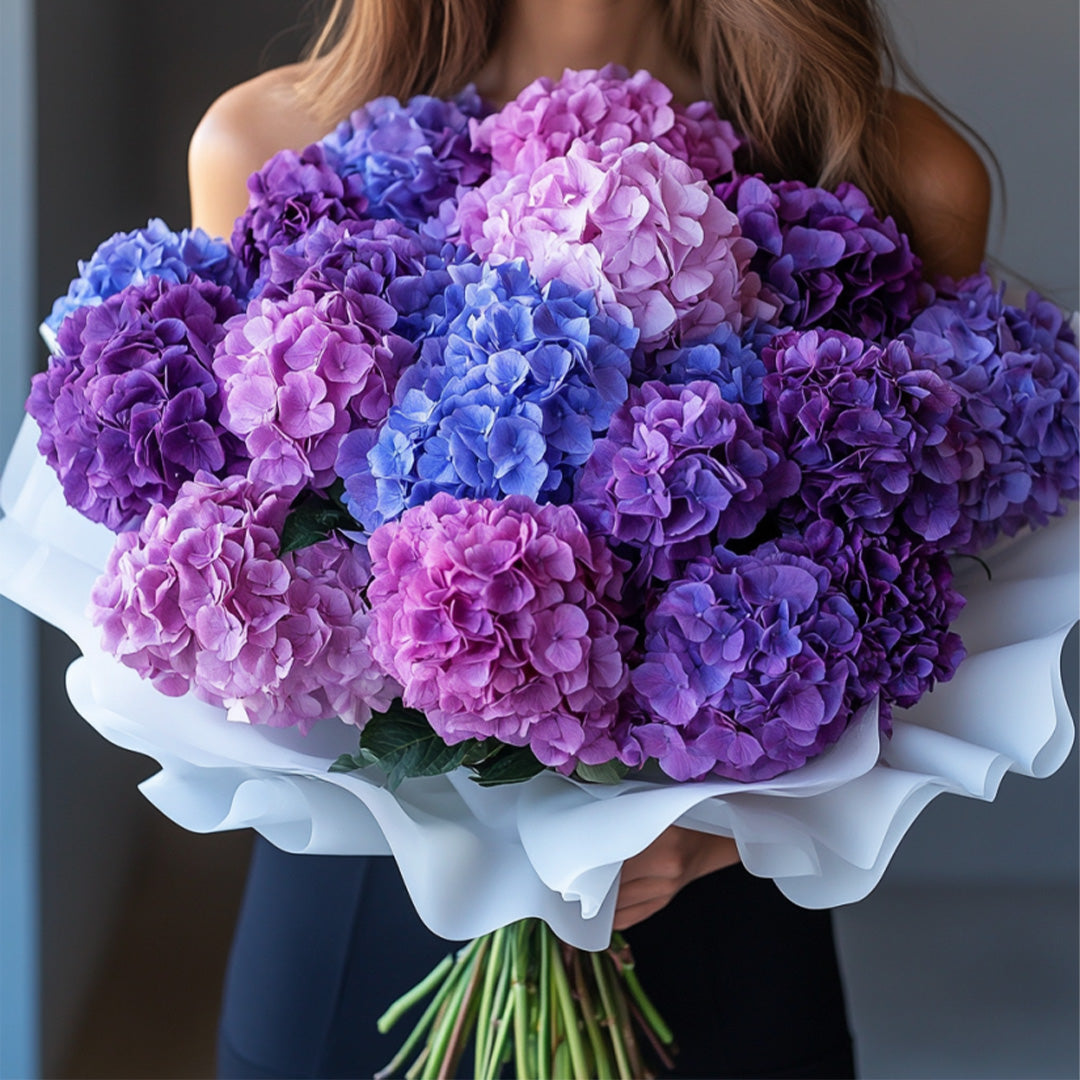 Pastel hydrangea bouquet in shades of purple, pink, and blue, wrapped in elegant white paper — luxury floral arrangement by Flowers Lounge by Iness