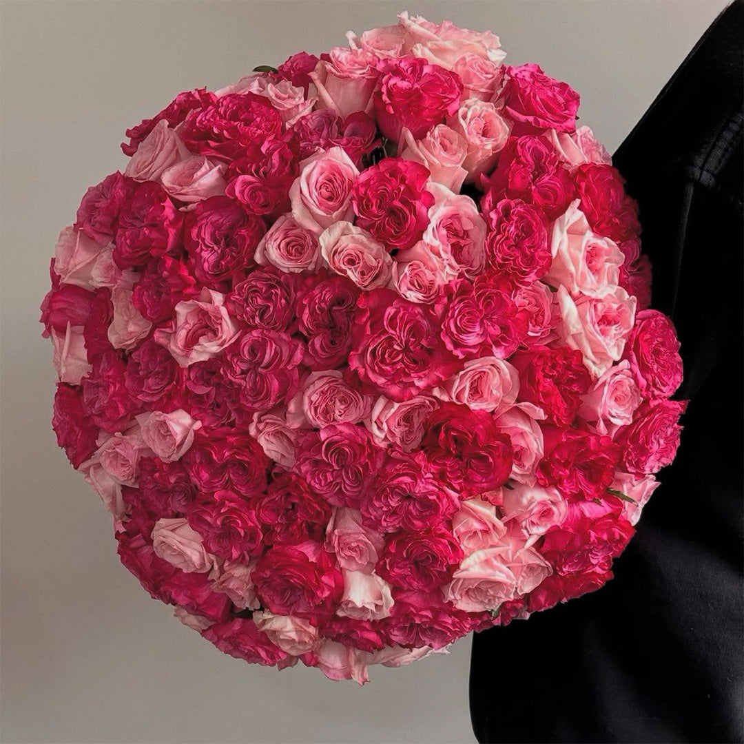 A large bouquet of mixed roses in shades of pink and red, tightly arranged in a spherical form. The roses are delicately arranged, with the vibrant pink tones contrasting beautifully with the soft red hues, creating a stunning and romantic floral arrangement.