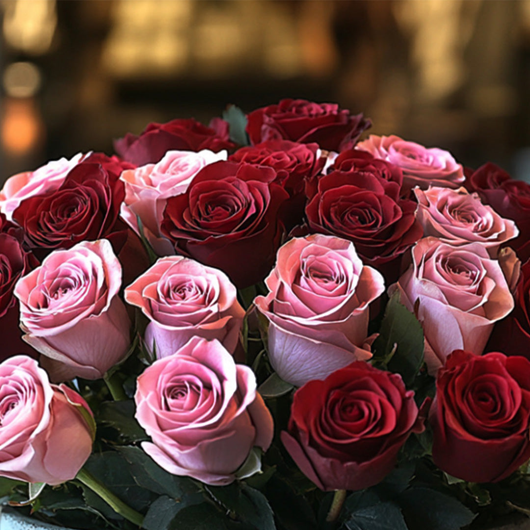 A close-up view of a rose bouquet featuring deep red and soft pink roses, arranged elegantly in a circular shape with lush green foliage.