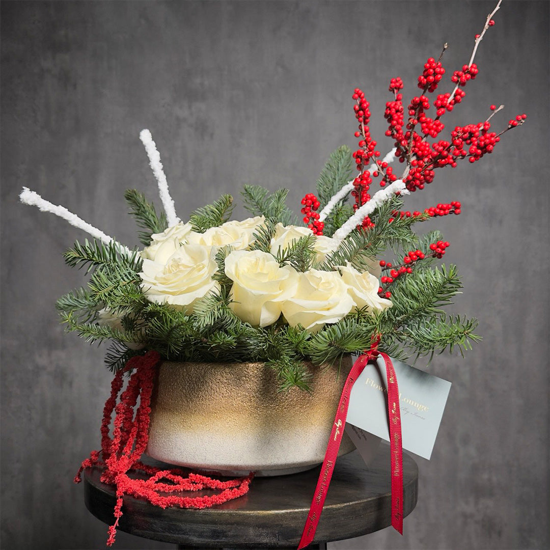 Festive arrangement of white roses with red berries and winter greens in a gold ceramic vase – perfect for Christmas or holiday décor.