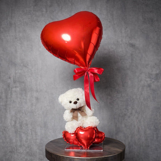 White teddy bear holding red heart balloon on a decorative base – romantic gift arrangement.