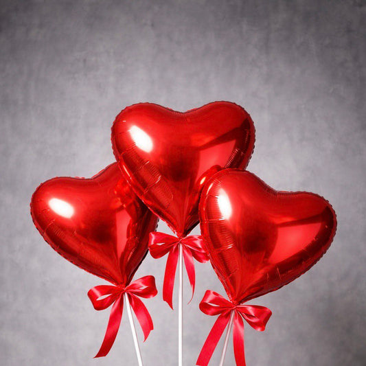 Three red heart foil balloons on white sticks, each tied with a red satin ribbon – romantic gift accessory.