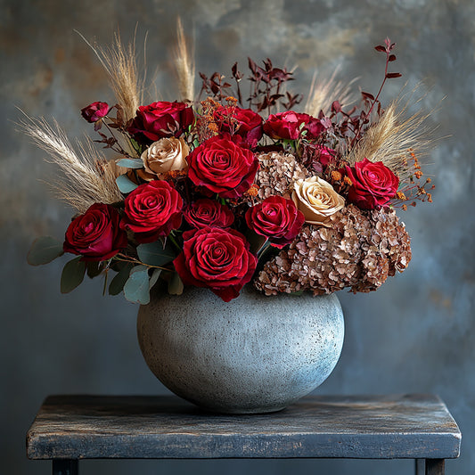 A luxurious and elegant floral arrangement featuring rich red roses, soft cream roses, dried florals, and pampas grass. This beautifully balanced bouquet, presented in a textured ceramic vase, evokes a sophisticated, timeless charm, perfect for special occasions or a heartfelt gift.