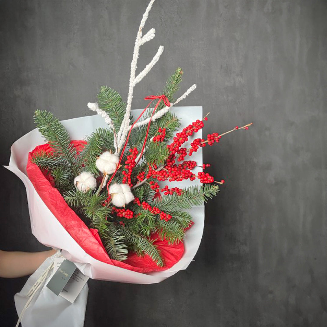 Holiday bouquet with pine branches, red berries, and cotton stems wrapped in white and red paper – Winter Cheer by Flowers Lounge
