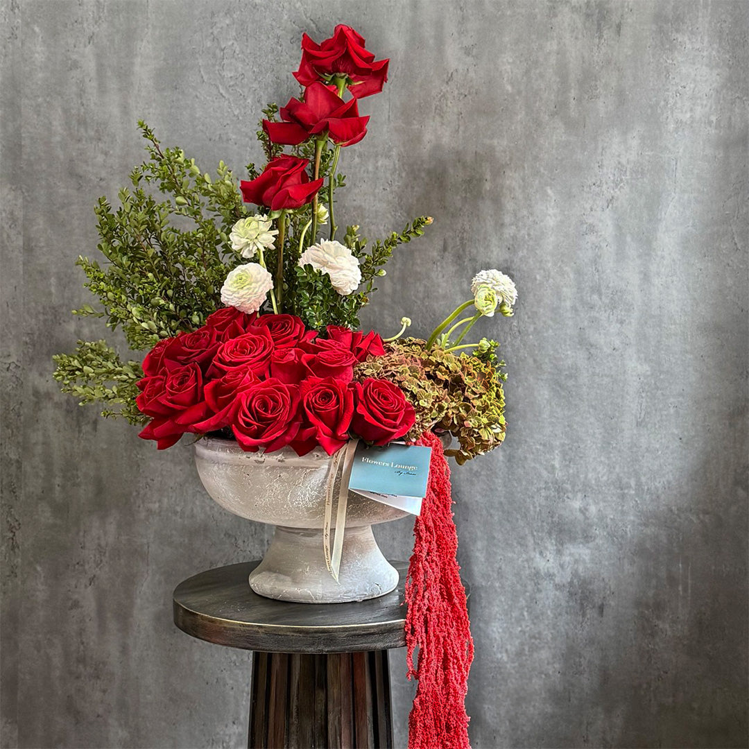 Luxury floral arrangement with vibrant red roses, white ranunculus, and green foliage in an elegant stone vase. Perfect for special occasions such as Valentine’s Day, anniversaries, or romantic gestures, with a sophisticated ribbon tied around the arrangement.