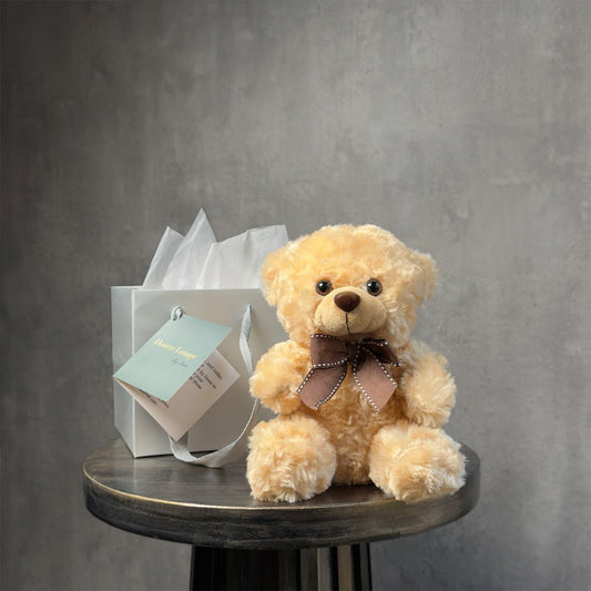Plush brown teddy bear with a satin bow and a luxury gift bag on a round table, ideal for gifting.