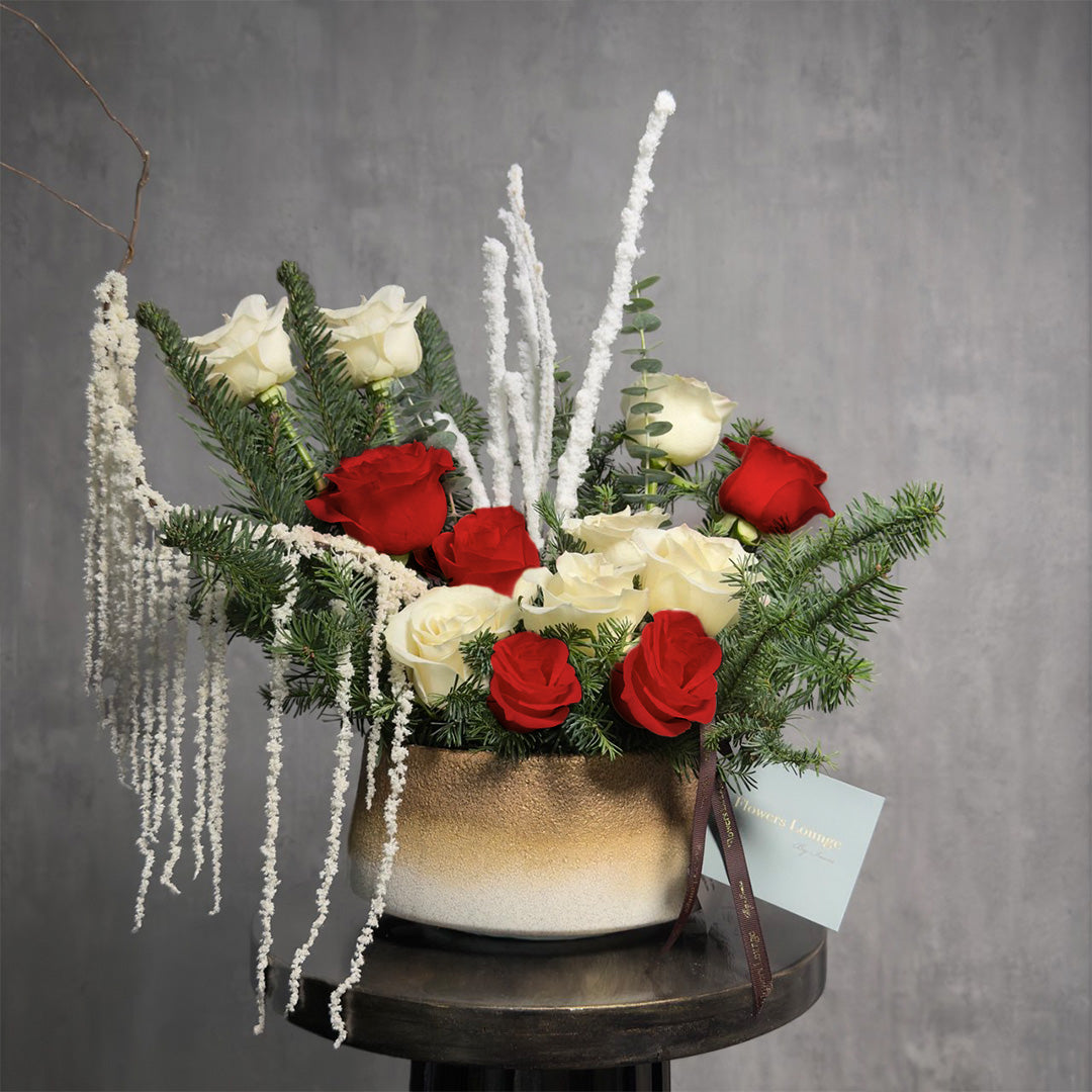 Red and white rose Christmas floral arrangement with pine and eucalyptus in a gold ceramic vase