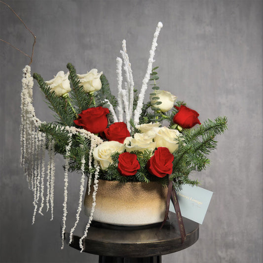 Red and white rose Christmas floral arrangement with pine and eucalyptus in a gold ceramic vase